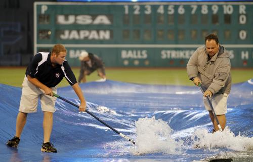 日米大学野球第２戦が雨天順延となり、グラウンドを覆うシートの上にたまった雨をかき出す球場スタッフ