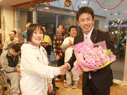 車椅子を寄付するため福島県の社会福祉法人を訪ねた赤星氏（右）は花束を贈られ歓迎される