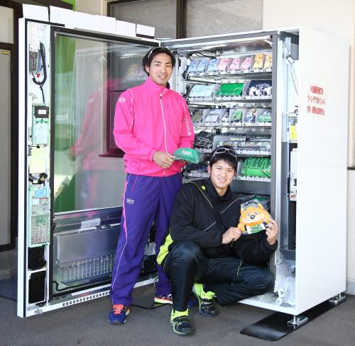 期間限定で鎌ケ谷スタジアムに登場したファイターズ「グッズが買える自動販売機」に商品を補充する屋宜（左）と大谷