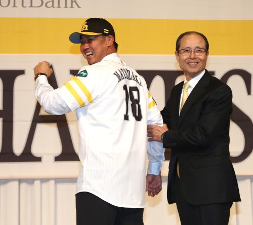背番号「１８」のユニホームに袖を通し笑顔を見せる松坂。右は王会長