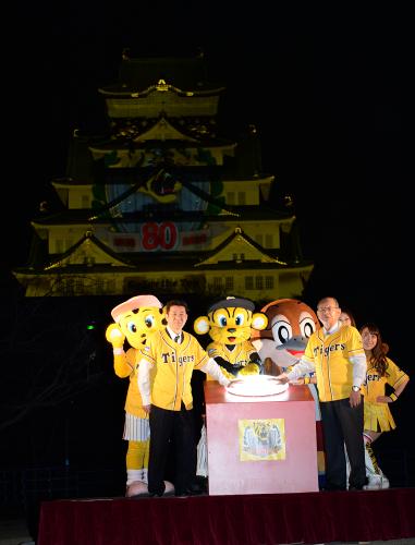 球団創設８０周年記念のロゴが浮かび上がった大阪城をバックにポーズをとる（左から）松井大阪府知事、吉田氏