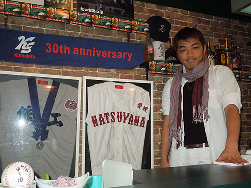 スポーツバー「たっちあっぷ」を経営する星子崇さん、店内には熊本工と松山商のユニホームが並んで飾られている