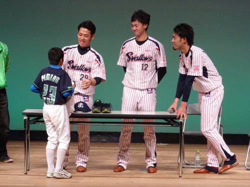 プレゼント抽選会で、山田のＴシャツを着た少年に自身のグッズを手渡すヤクルト・小川（左）。中央は石山、右は秋吉