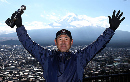 ２０１５年の隠しマイク大賞に輝き、富士山をバックにトロフィーを掲げる田辺監督