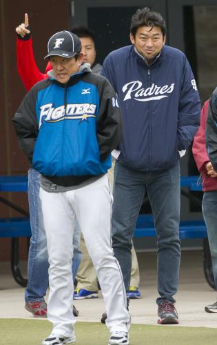 極寒と雨の中、肩をすくめながらブルペンでの投球練習を見守る栗山監督（左）とパドレス・斎藤隆氏