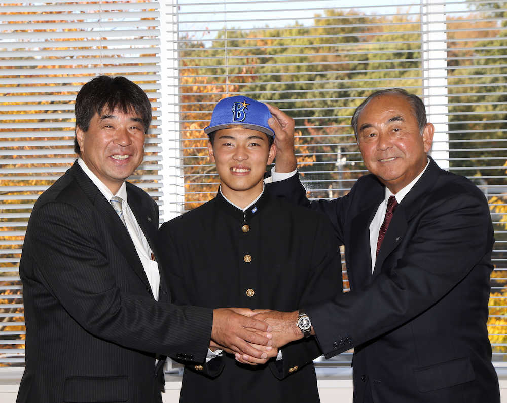 吉田スカウト部長（右）に帽子を被せてもらい笑顔を見せる桜井（中央）。左は欠端スカウト