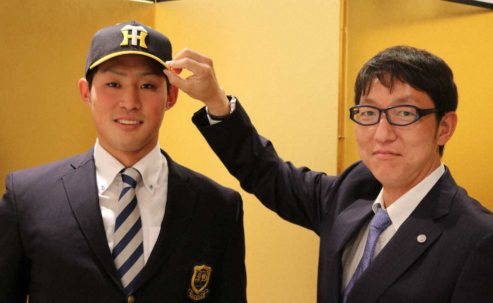 阪神との仮契約交渉を終え、吉野スカウト（右）から帽子をかぶせてもらう上武大・佐藤蓮（阪神球団提供）
