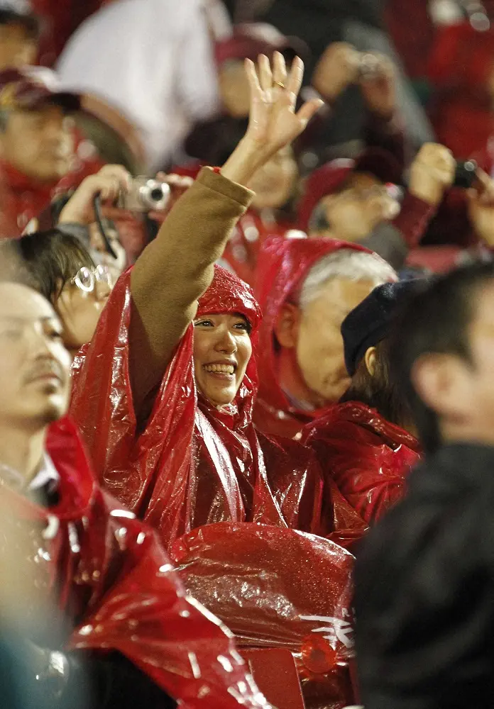 2013年日本シリーズで冷たい雨が降りしきる中、楽天カラーのカッパを着て笑顔で応援するまい夫人