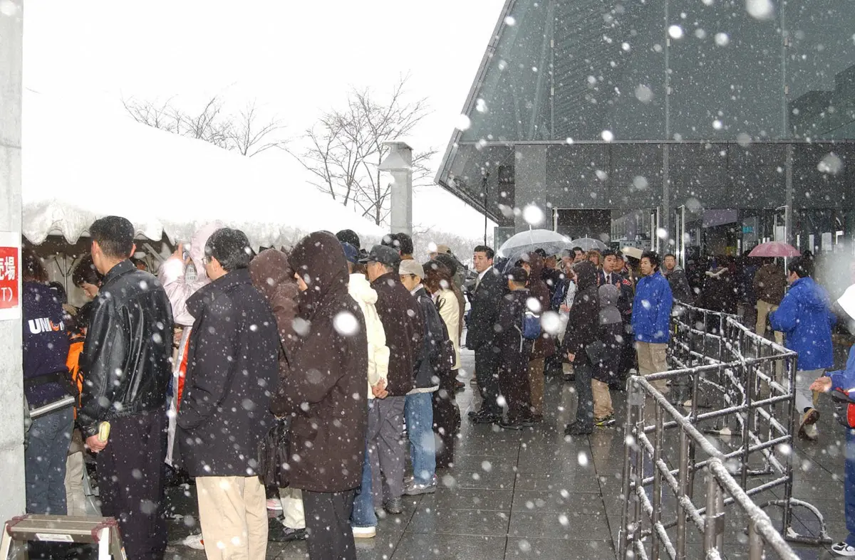 札幌ドームの外で雪の降る中、当日券を求めるファンの長い列