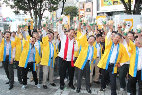 長野県中野市のキノコ生産者とともに「１、２、３、ダー！」の掛け声で気勢をあげるアントニオ猪木（中央）