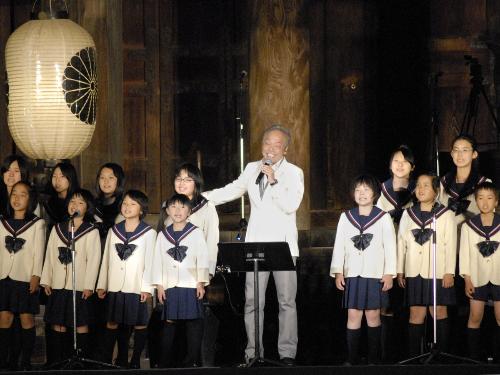 長野市・善光寺の本堂前で、長野少年少女合唱団とともに歌う歌手の谷村新司
