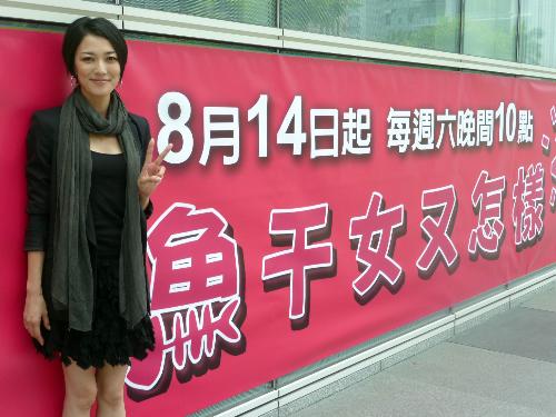 台北市内の「ホタルノヒカリ2」の看板の前に立つ板谷由夏。看板の文字は中国語のタイトルで「干物女で何が悪いの？」の意味