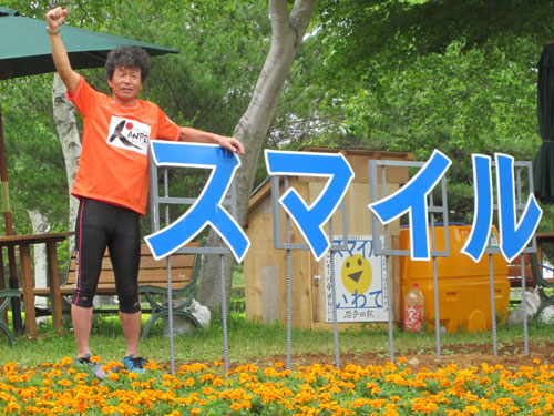 岩手県宮古市で行われた復興イベントで、東日本大震災の被災地マラソン挑戦を発表した間寛平は、自ら苗を植えた花畑に掲げられた「スマイル」の看板とともにガッツポーズ
