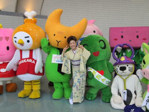 東京・代々木公園で開かれた「九州観光・物産フェア」で、九州各地のゆるキャラを従えて新曲「おもいでの宿」を歌唱した中村美律子