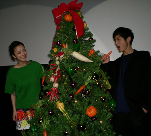 野菜が飾られたクリスマスツリーを贈られ、喜ぶ上戸彩（左）と、ニンジンを口に運ぶ高良健