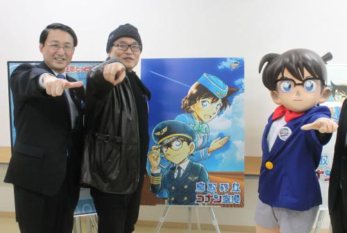 「鳥取砂丘コナン空港」のロゴを用いたポスターの前で、ポーズを決める作者の青山剛昌さん（右）と平井伸治知事