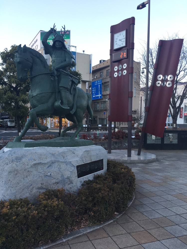 上田駅前の真田幸村像。銅像のうしろには六文銭のノボリを型どった時計塔が建つ
