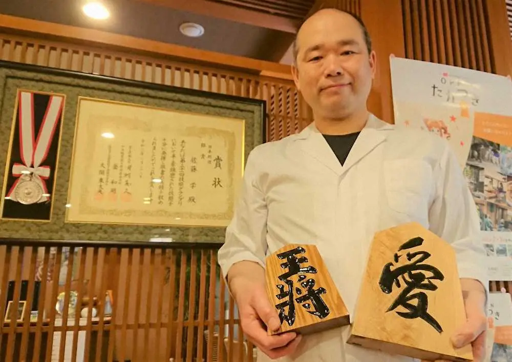 「技能グランプリ」の銀メダリストの賞状とメダルの前で微笑む山水館の佐藤学料理長