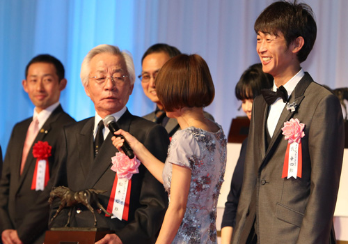 授賞式の壇上で凱旋門賞挑戦を宣言した松本オーナー。右は武幸