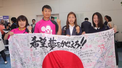 応援メッセージが書かれた日本国旗を手に笑顔を見せる（左から）母・秀子さん、父・圭永さん、奥原、姉・未来さん