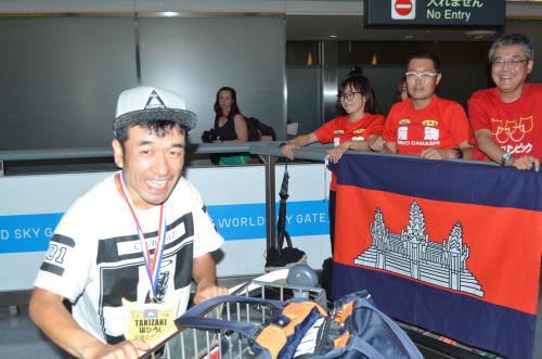 成田空港に到着した猫ひろし。ランナー仲間らがカンボジア国旗を広げて出迎えた