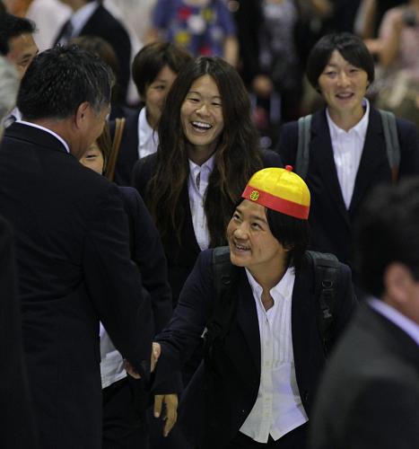 中国で買った？帽子をかぶって日本サッカー協会・田嶋副会長（左背中）と握手をする大野（手前）を見て、笑顔の沢