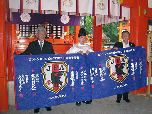上田女子委員長（左）が必勝祈願で訪れ、祈念してもらったなでしこジャパンの旗（中央は熊野速玉大社の神官、右は熊野三山協議会会長で新宮市長の田岡実千年氏）