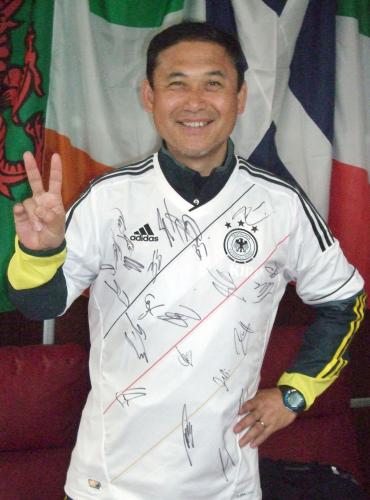 サッカー男子ドイツ代表のサイン入りユニホームを着て、笑顔を見せる佐々木監督