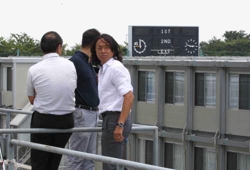 福島Ｊヴィレッジを視察する北沢理事（右）らの奥では、震災のときに止まったままの掲示板の時計が見える
