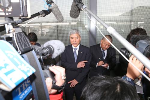 成田空港に到着した大仁会長は大勢の報道陣に囲まれる