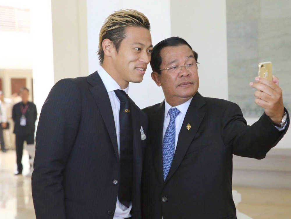 カンボジアのフン・セン首相(右）とスマートフォンで自撮りをする本田（カンボジア首相府提供）