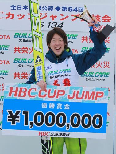 優勝賞金１００万円のボードを手に笑顔の小林
