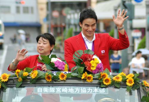 パレードで手を振る、ロンドン五輪競泳で二つのメダルを獲得した松田丈志。左は久世由美子コーチ