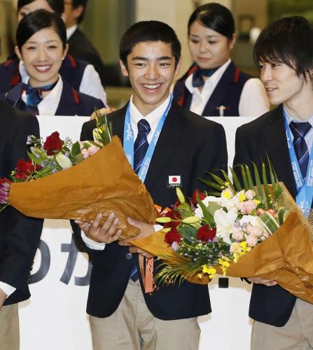 体操の世界選手権から帰国し、花束を手に笑顔の白井健三選手。右は内村航平選手