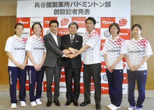 手を取り合う熊本県の蒲島郁夫知事（中央）、再春館製薬所の西川正明社長（左から３人目）、ルネサスバドミントン部の選手ら