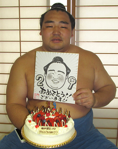 報道陣から贈られた誕生日ケーキと似顔絵を手にする鶴竜