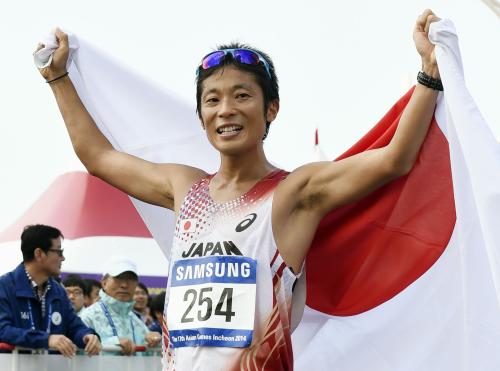 男子50キロ競歩で優勝し、笑顔で日の丸を背にする谷井孝行