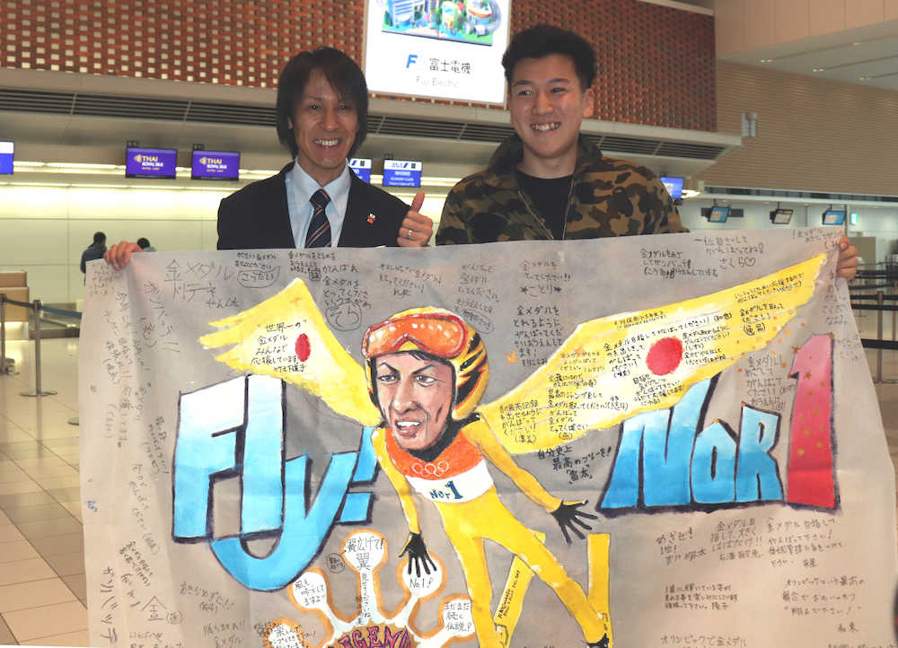 飯舘村から新千歳空港に駆けつけた渡辺さん（右）に寄せ書き入り横断幕を手渡され、笑顔