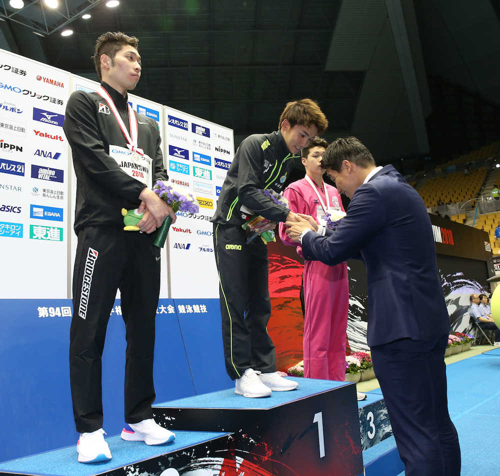 第９４回日本選手権水泳競技大会１日目、江原（右）が松田氏（同手前）から表彰を受ける中、立ち尽くす萩野