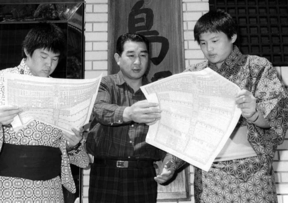 １９８８年４月、父親の藤島親方（中央）とともに、番付に初めて載った自分の名前を確かめる若花田（左）と貴花田