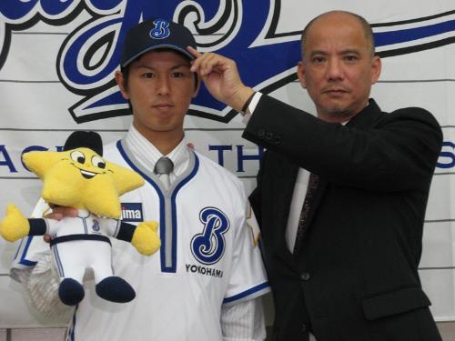 仮契約を終えた須田（左）は河本取締役から帽子を被せられる