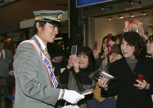 福岡市営地下鉄博多駅の一日駅長に就任し、ＰＲグッズを配る福岡ソフトバンクホークスの和田毅投手（左）