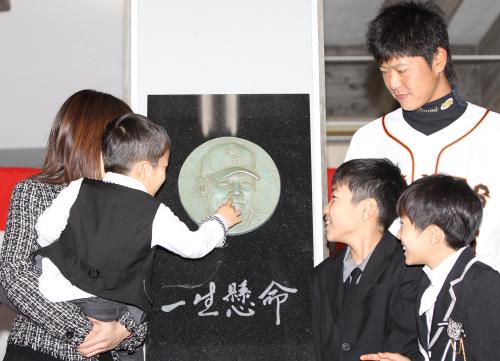 木村拓也氏の母校・宮崎南高校で行われた顕彰レリーフ除幕式の最後に行われた記念撮影終了後、二男の俊生くん（左から２人目）がレリーフの顔が気になり指で触りだす