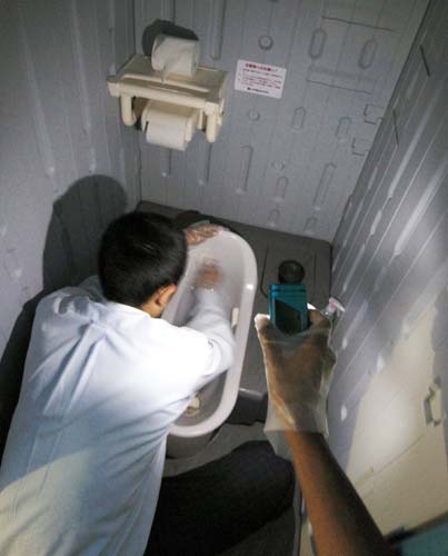 携帯電話の液晶の明かりを頼りに仮設住宅地のトイレ掃除をする高田高ナイン