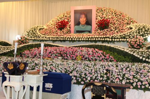 花で飾られた仁美夫人の祭壇。遺影の両側には真っ赤なバラが