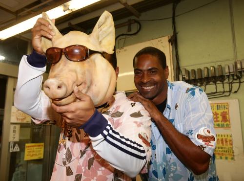 牧志公設市場の精肉店に飾られた豚のキャサリンの頭をかぶる巨人・ロペス（左）とニヤニヤするアコスタ