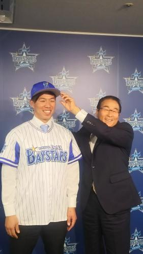 横浜市内の球団事務所で入団会見を行い、ＤｅＮＡの高田ＧＭから帽子をかぶせられる藤岡