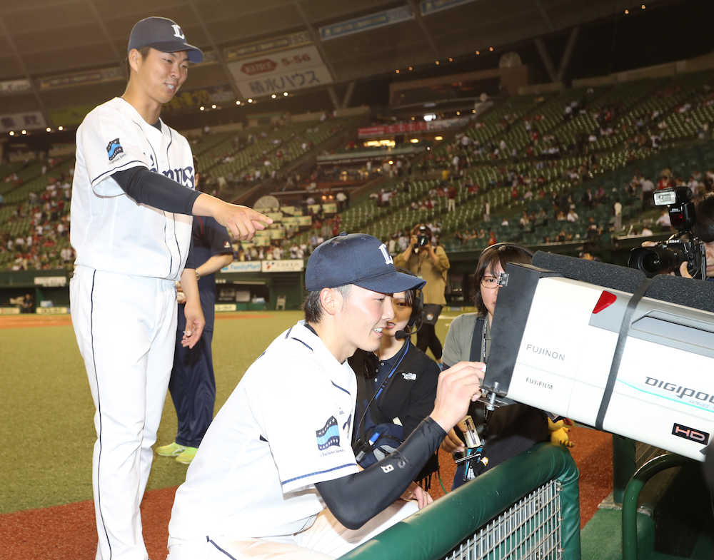 テレビカメラのレンズにサインをする西武・源田（右）と十亀