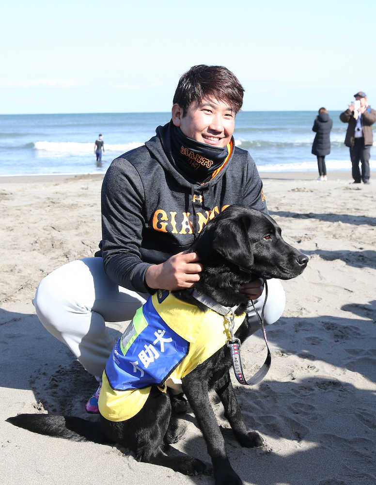 社会貢献活動を行った菅野は海岸でサーファーの介助犬と笑顔を見せる
