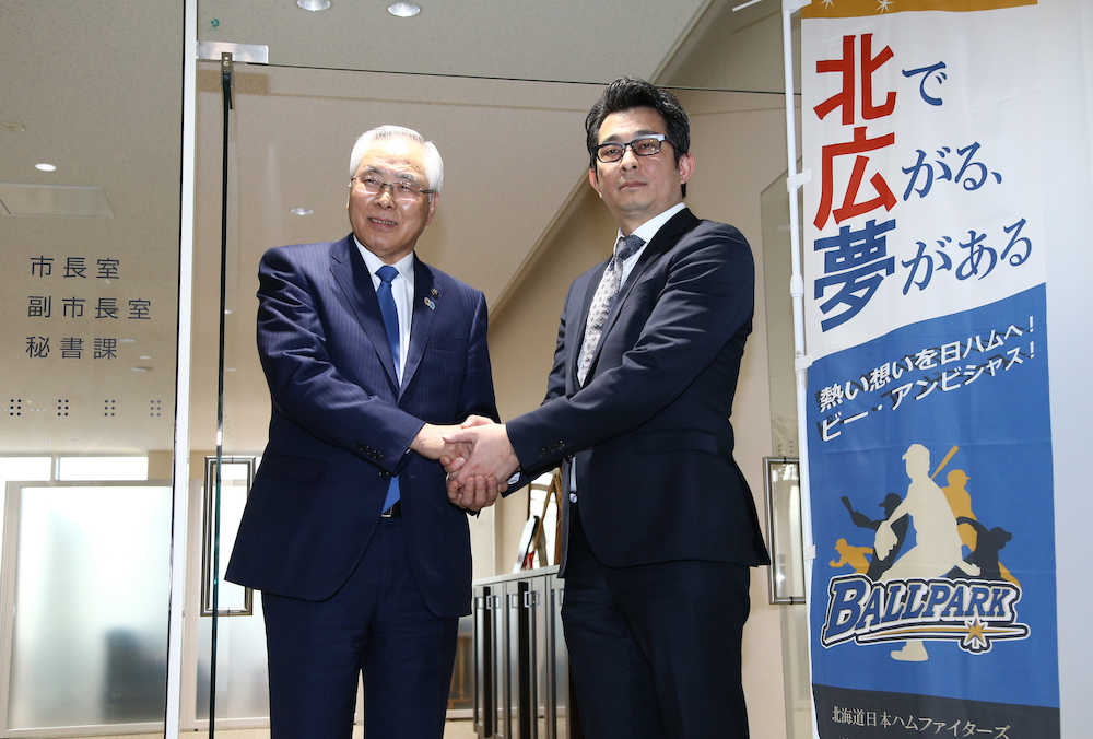 北広島市役所訪問後、上野正三市長（左）と握手を交わす日本ハムの前沢賢・事業統括本部長